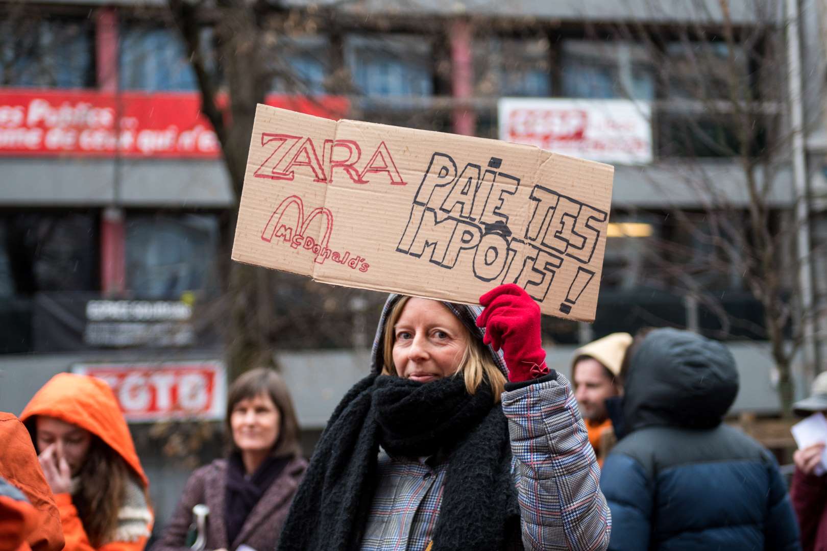 Une femme portant une pancarte durant une action pour plus de justice fiscale. Zara, Mc Donald, payez vos impôts